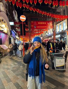 a woman is standing on the street talking on her cell phone while wearing a blue hat and scarf