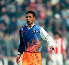 a soccer player in blue and orange uniform on the field with his hand out towards the ball