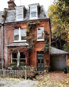 an old brick house with ivy growing on it's windows and door, surrounded by autumn leaves