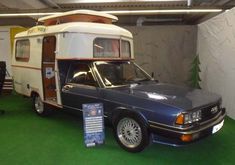 an old camper parked in a garage next to a car and a trailer on display