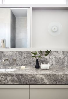 a bathroom with marble counter tops and white cabinets, along with a black vase filled with flowers