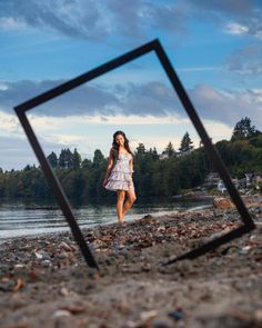 a woman in a white dress is walking on the beach with her reflection in a mirror