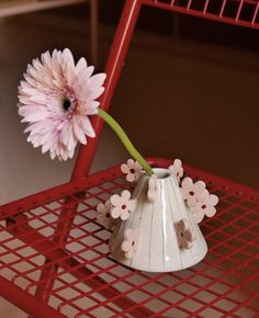 a pink flower in a white vase sitting on a red chair with metal grating