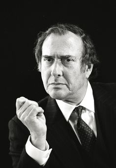 a black and white photo of a man in a suit holding his fist up to the side