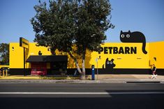 a yellow building with a black cat painted on it's side and a person walking by