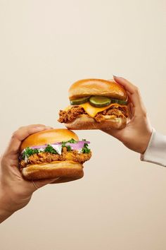 two hands holding sandwiches with meat, cheese and cucumber on them in front of a white background