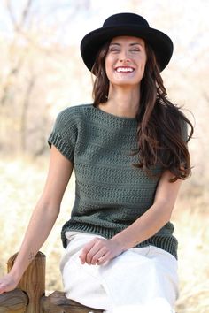 a woman sitting on a wooden fence wearing a black hat and green knitted sweater