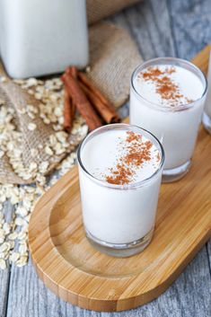 two glasses filled with milk sitting on top of a wooden tray next to cinnamon sticks