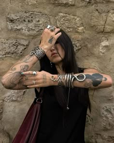 a woman with tattoos on her arms and armbands is posing in front of a stone wall