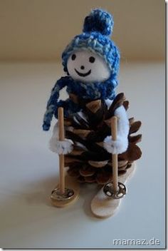 a knitted snowman sitting on top of a pine cone and holding a shovel