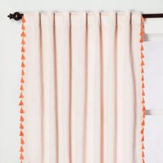 an orange and white curtain with tassels hanging on the side of a window