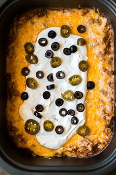 an enchilada casserole with olives and sour cream on top