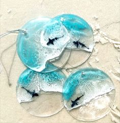 three glass coasters with birds on them sitting in the sand and one has a string attached to it