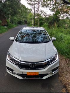 a white car parked on the side of a road in front of some grass and trees