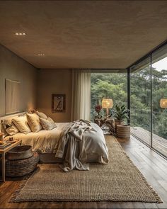 a bedroom with a large bed and lots of windows overlooking the trees in the distance