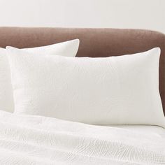 two white pillows sitting on top of a brown headboard next to a pillow case