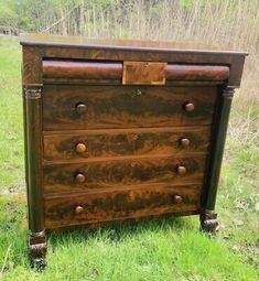 an antique chest of drawers sitting in the middle of a grassy field with trees in the background