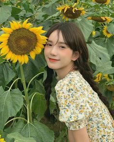 a woman standing in front of a sunflower field with her long hair pulled back