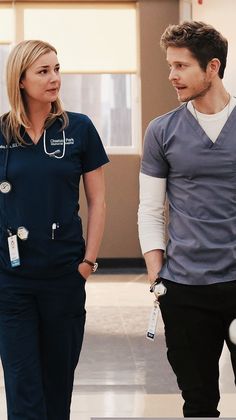 a man and woman in scrubs are talking to each other while walking through an airport