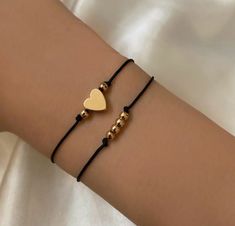 two bracelets with gold hearts and beads are on the arm of a woman wearing a white shirt