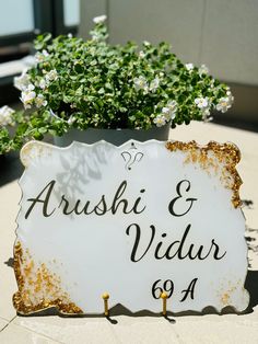 a white sign sitting on top of a table next to a planter filled with flowers