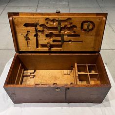 an open wooden box with tools inside on a white cloth covered flooring area next to a sidewalk