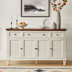 a white buffet table with flowers and plates on it in front of a framed painting