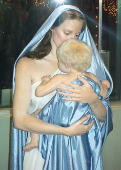 a woman in a blue dress holding a child wrapped in a silver cloth with fireworks behind her