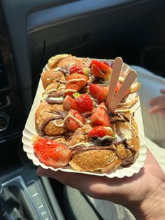 a person is holding up a plate of food in the car with strawberries on it