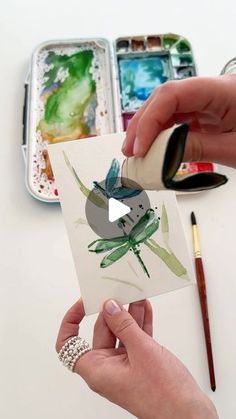 someone is painting flowers with watercolors on the paper and then using a brush