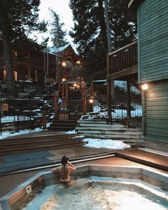 a woman sitting in an outdoor hot tub with stairs leading up to the house and trees