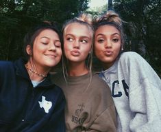 three girls are posing for the camera with trees in the background