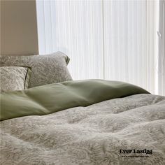 an unmade bed in front of a window with white vertical blinds and green comforter