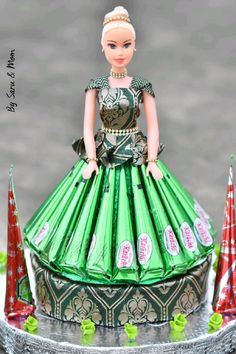 a doll is standing on top of a cake with green and red decorations around it