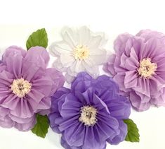 purple and white paper flowers with green leaves on them are arranged in a horizontal arrangement