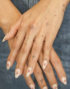 a woman's hands with stars and numbers tattooed on their fingers, both holding each other