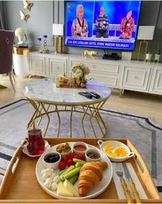 a tray with food on it in front of a television set and table with utensils