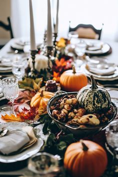 a table set for thanksgiving dinner with pumpkins and gourds in the center