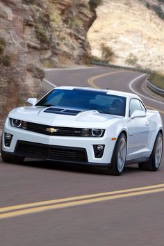 a white chevrolet camaro is driving down the road