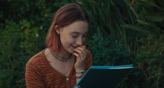 a woman sitting in front of a book with her hand on her face and looking at the screen