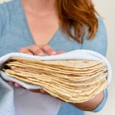 a woman holding a stack of tortillas in her hands