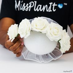 a person holding a white vase with flowers in it's hands and wearing a black t - shirt