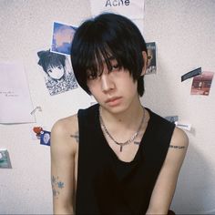 a young man with black hair and piercings sitting in front of a white refrigerator