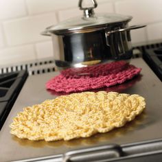 two crocheted sponges are sitting on the stove top next to a pot holder