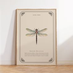 a framed poster with a dragonfly on it in front of a white wall and wooden floor