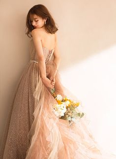 a woman in a long dress is holding a bouquet and leaning against a wall with her back to the camera