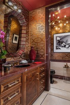 an ornate bathroom with gold and red wallpaper, marble counter tops and wooden cabinets