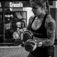 a woman with tattoos wearing boxing gloves and holding a punching mitt in her hand