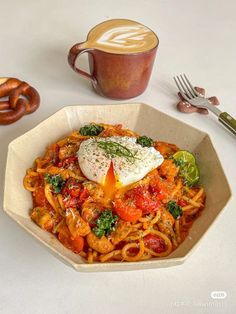 a bowl filled with pasta and vegetables next to a cup of coffee