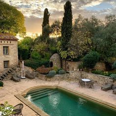 an outdoor swimming pool surrounded by stone walls and greenery, with tables and chairs around it